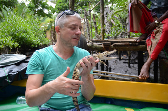 A man holds in hands a small crocodile. Jungle of Sri Lanka