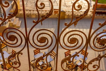 Fototapeta na wymiar Outdoor restaurant seen from above with empty tables through a metal railing, wrought in an elaborate fashion with spirals and curves 
