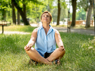 Beautiful mature woman meditating in green park