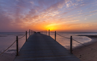 Fototapeta na wymiar Pier reaching into the Egyptian sea at sunset with a backdrop of clouds and golden setting sun