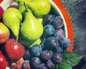 Ripe green pears, red apples and plums in a plate on a wooden surface with grunge texture, close up, top view  