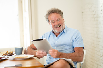 Handsome senior retired old man using tablet with joy while having breakfast at home