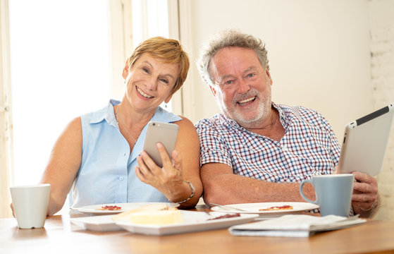 Happy senior couple using smart phone and tablet while having breakfast