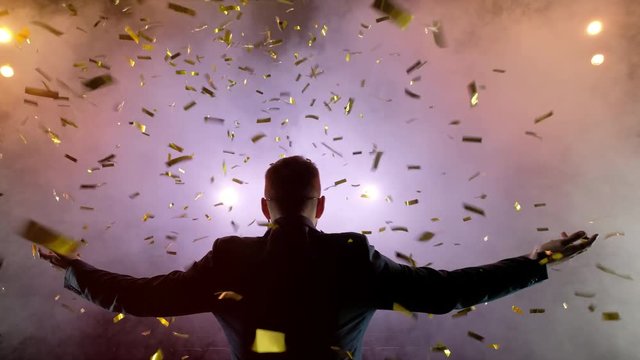 Successful businessman with arms up celebrating his victory. Celebrating success. Low angle view of excited young businessman keeping arms raised and expressing positivity while stands on the stage in