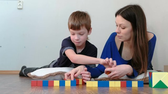 Mom and son playing together with wooden colored education toy blocks lying on the floor. Son takes the wooden cubes from his mother.