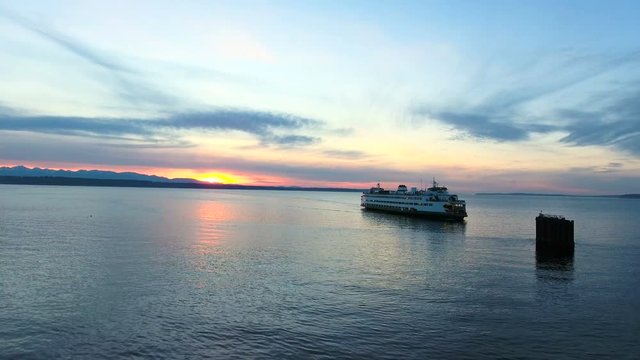 A Washington State Ferry arrives at the Edmonds, Washington ferry dock with the Olympic Mountains as a backdrop at sunset.