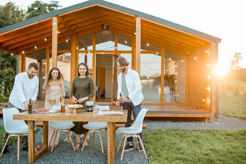 Happy friends carrying food preparing for the dinner on the backyard of the modern wooden house during the sunset