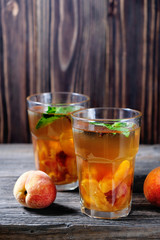 Summer cold drinks: homemade peach sangria with ice cubes, and mint in glass on wooden background
