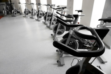 Modern gym interior with equipment. Row of training exercise bikes detail, backlight. Healthy...