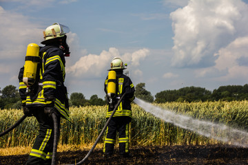 Zwei Feuerwehrleute löschen unter schwerem Atemschutz einen Feldbrand.