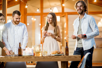Friends having a dinner with pizza on the backyard of the modern house decorated with lights during the evening time outdoors