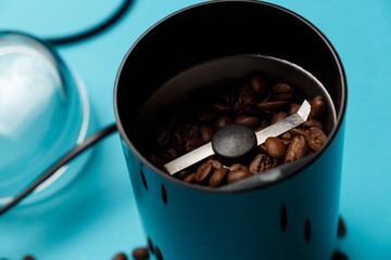 Electric coffee grinder with roasted coffee beans on the kitchen table with blue tabletop. Close-up