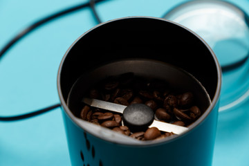 Electric coffee grinder with roasted coffee beans on the kitchen table with blue tabletop. Close-up