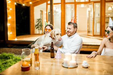 Funny dog with young couple sitting at the table during a celebration on the backyard of the house outdoors