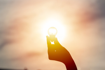 Idea and creativity concept. Silhouette hand holding light bulb with solar energy. New ideas...