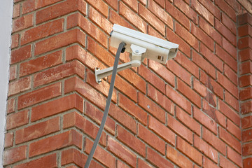 Surveillance camera attached to a brick wall overlooking a parking lot