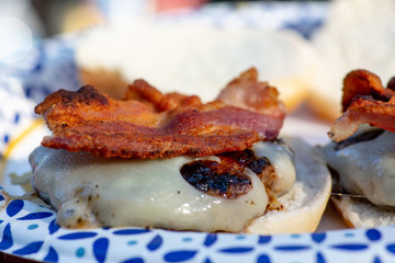 For dinner a bacon and Swiss cheeseburger on a white a blue paper plate at the campground.