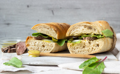 Roast beef sandwich with fresh salad, onion and cukes and mustard sauce on white wood cutting board