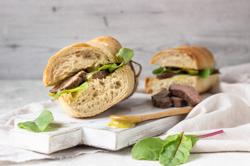 Roast beef sandwich with fresh salad, onion and cukes and mustard sauce on white wood cutting board