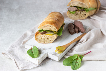 Roast beef sandwich with fresh salad, onion and cukes and mustard sauce on white wood cutting board
