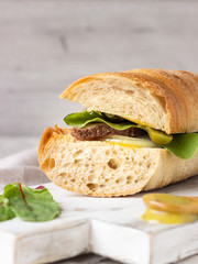 Roast beef sandwich with fresh salad, onion and cukes and mustard sauce on white wood cutting board