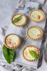 Mini tartlets with cream cheese filling and salmon on white wooden cutting board.