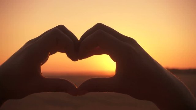Silhouette of girl hands making heart symbol at sunset