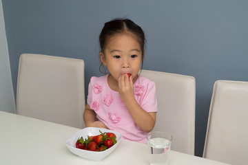 .The girl is eating strawberry in the kitchen.