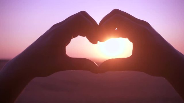Silhouette of girl hands making heart symbol at sunrise