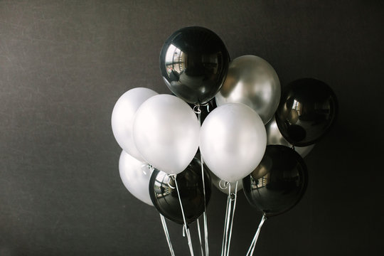 Black and white balloons on a dark black background. Celebration concept / White and black balloons on a dark black background for a holiday, birthday or other holiday. Photo for posters or postcards.