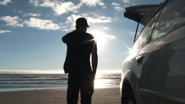 Model released person standing next to car parked on sandy beach at the Oregon Coast on beautiful day with bird flying by and sun shining bright.