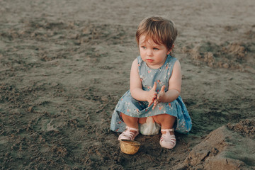 Little caucasian girl have fun digging in the sand at ocean beach, building sand castle.