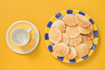 Teacup and plate with pita bread on yellow background