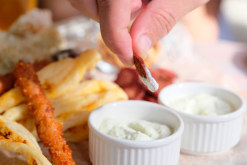 Man's hand dips a snack in sauce