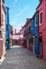 Fototapeta na wymiar One of the numerous streets of the island of Burano, near Venice with the homeland of colorful houses - the visiting card of the island, Italy