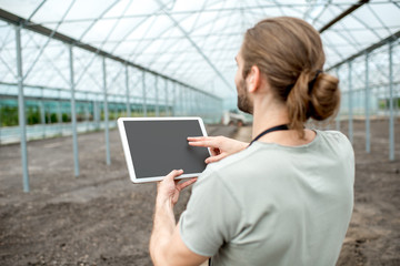 Farmer working with digital tablet with empty screen to copy paste standing in the glasshouse