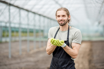 Portrait of a handsome farmer with mineral fertilizers standing in the glasshouse with cultivated...