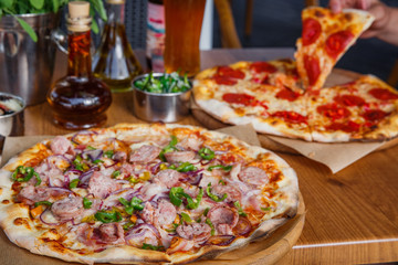Hot delicious pizza with sausage, paprika and red onion on wooden restaurant table.