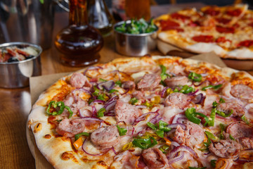 Hot delicious pizza with sausage, paprika and red onion on wooden restaurant table..