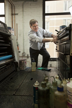 Business owner smiling and working with industrial printing machines inside an office in New York City, USA