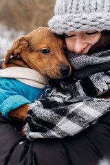 stylish hipster girl hugging and caressing cute puppy in snowy cold winter park. moments of true happiness. adoption concept. save animals
