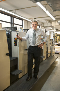 Business owner smiling and standing in front of a row of machines inside an office in New York City, USA
