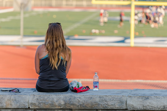 A young lady is sitting on a concrete bench beside a football field