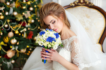 Portrait of beautiful bride with bouquet of flowers sitting on sofa, on background of Christmas tree