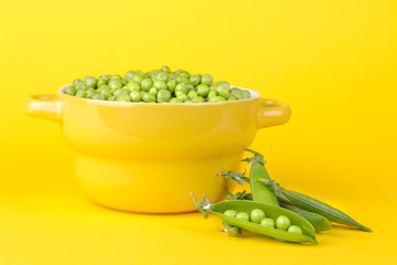 Fresh green peas in a yellow bowl next to peas in a stitch on a bright yellow background