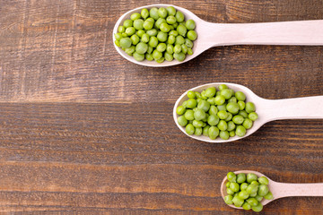 Fresh green peas in a wooden spoon on a brown wooden background. With place for inscription
