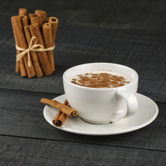 Close up white cup of salep milky hot drink of Turkey with cinnamon powder healthy spice on black wooden background
