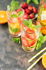 The glasses of lemon water. Lemonade with strawberry, mint and ice on a table. Sunny summer day. Copy spase