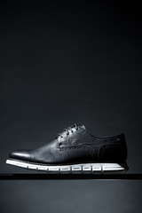 black leather shoe with white soles on a dark background, vertical