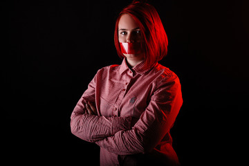 Red hair girl in dark studio with red color clothes, close portrait, woman in t-shirt and jeans. Face with Scotch tape on mouth. Censored theme